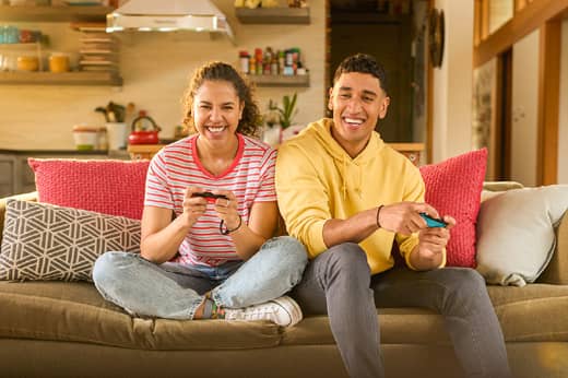 Two people are on a sofa playing Big Brain Academy: Brain vs. Brain on a Nintendo Switch system.