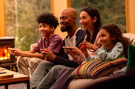 A family is cuddled together playing Big Brain Academy: Brain vs. Brain on a Nintendo Switch system.